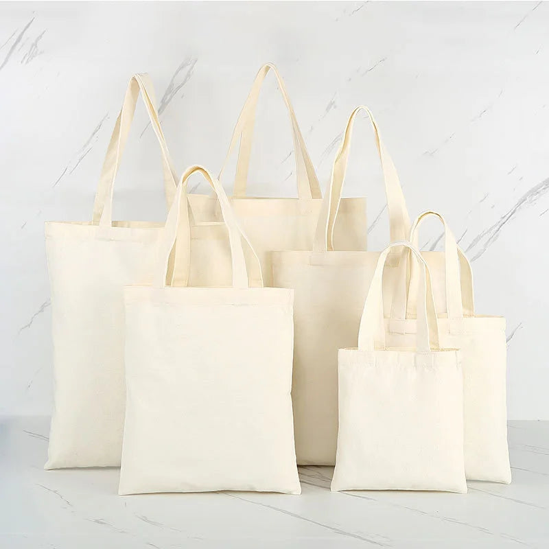 A collection of natural canvas tote bags in off-white and cream colors displayed on a white marble surface.
