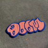 A decorative floor mat shaped like the letters MF OO UU, featuring pink and blue stitching.