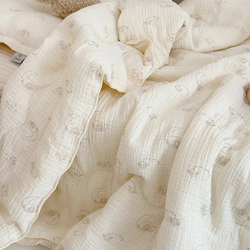 A soft, cream-colored muslin blanket with a subtle floral print is draped and folded.