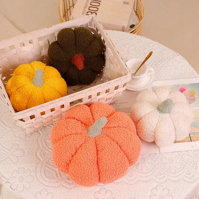 A collection of three 3D pumpkin-shaped throw pillows in yellow, dark green, and orange resting on a white lace tablecloth.