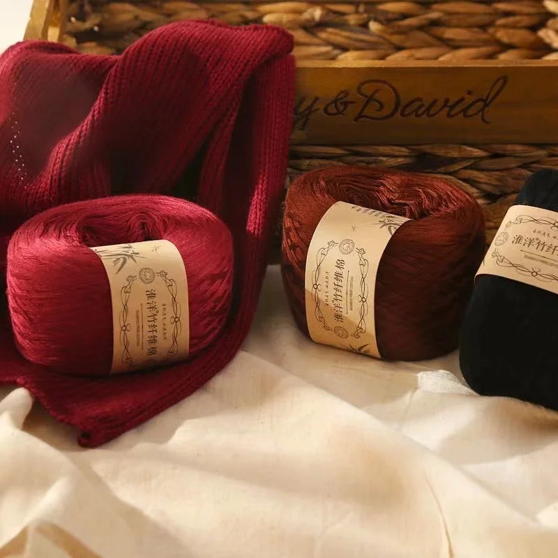 A close-up of deep red yarn rolled into a skein resting on white fabric next to a box of natural woven material.