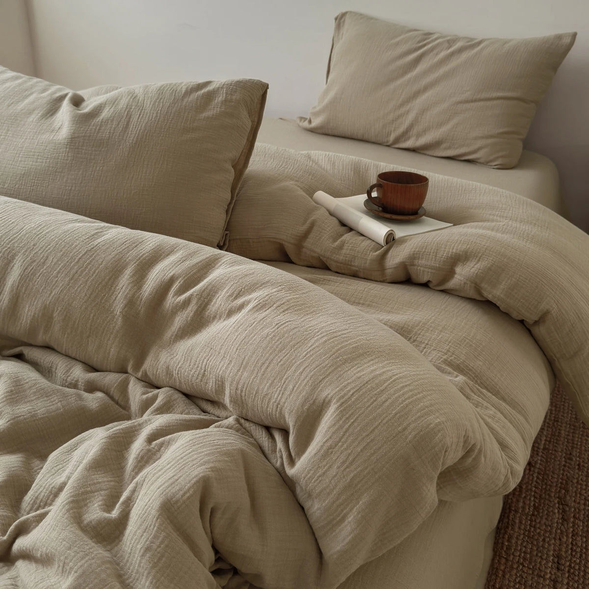 A beige soft 100% cotton duvet cover set with matching pillows and a small brown cup on the bed.