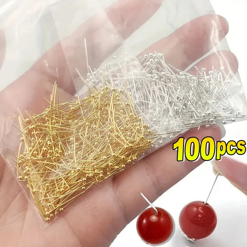 A hand holds a clear plastic bag containing 100 stainless steel ball head pins for jewelry making.
