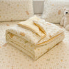A stack of cream-colored quilted blankets with a subtle floral pattern resting on a light-colored carpet.