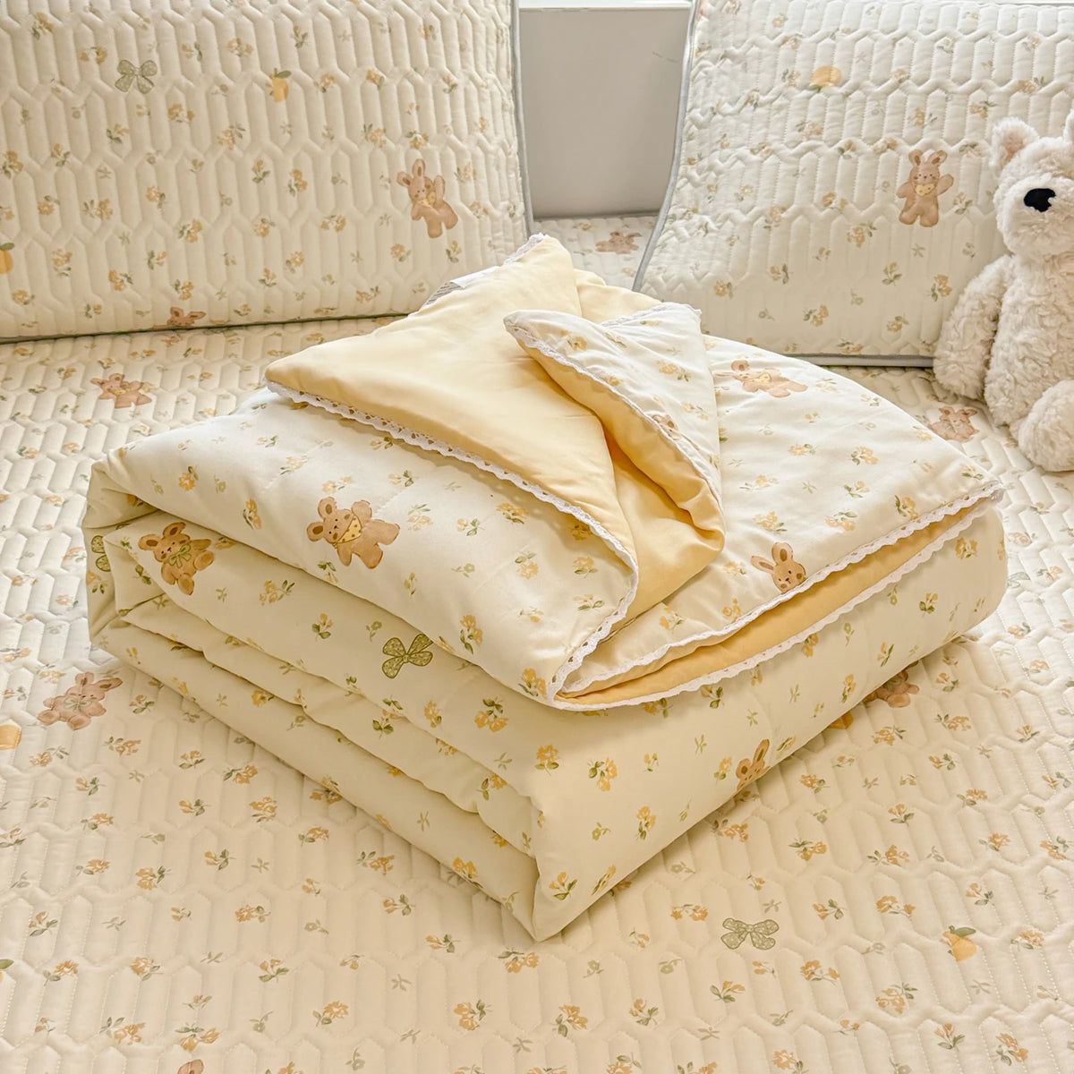 A stack of cream-colored quilted blankets with a subtle floral pattern resting on a light-colored carpet.