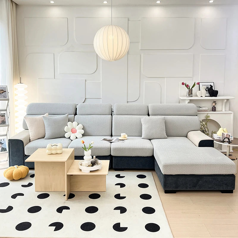 A modern light gray sectional sofa with a dark base and white decorative pillows in a bright living room.