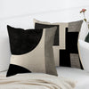 A modern abstract geometric throw pillow cover in black, white, and gray tones displayed on a white sofa.