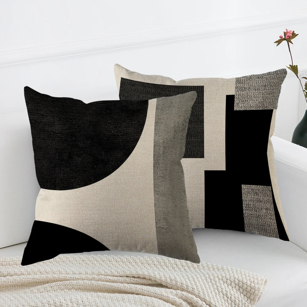 A modern abstract geometric throw pillow cover in black, white, and gray tones displayed on a white sofa.