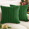 A deep emerald green square faux rabbit fur cushion cover resting on a light sofa next to festive holiday greenery.