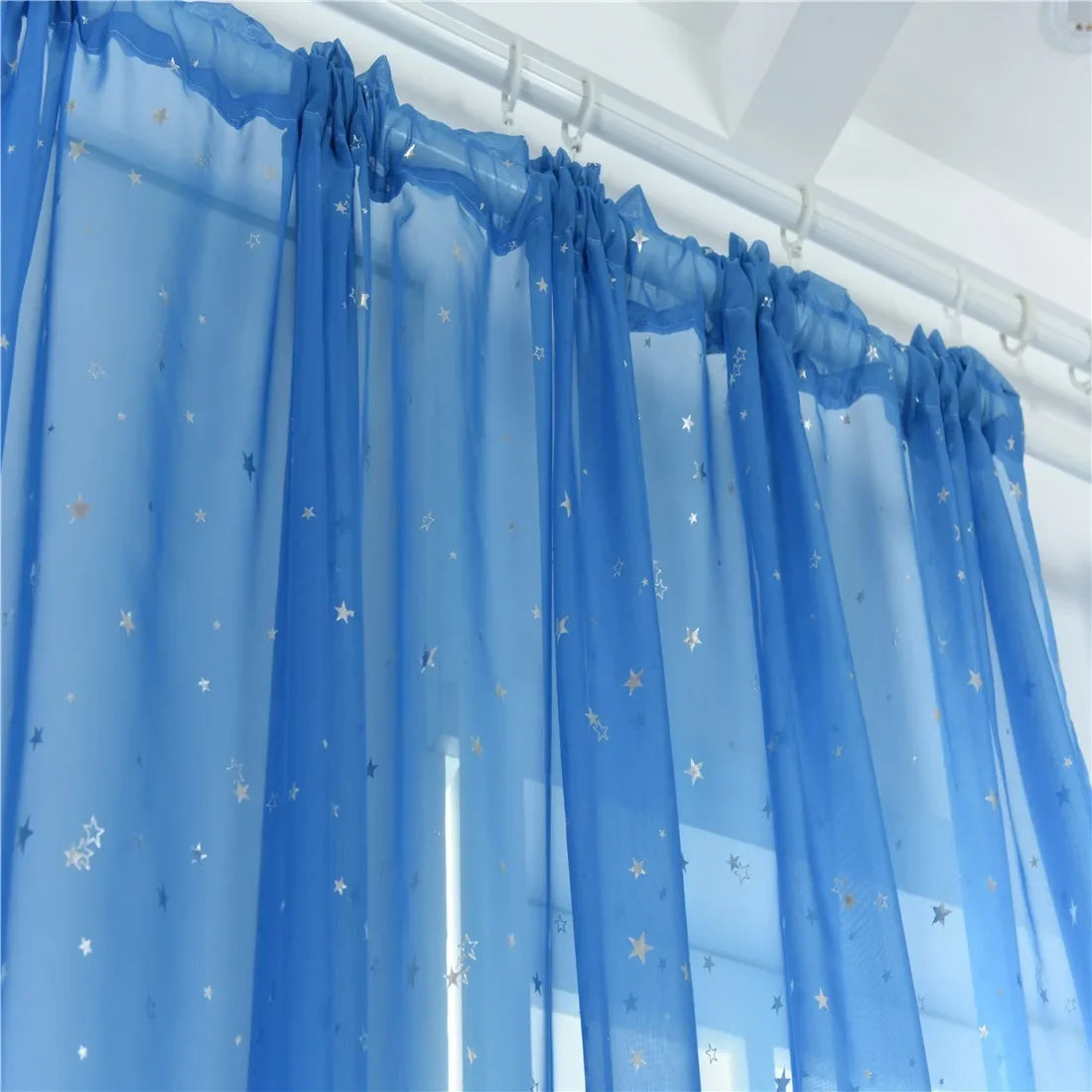 Light blue sheer tulle curtains decorated with silver stars hanging in a window.