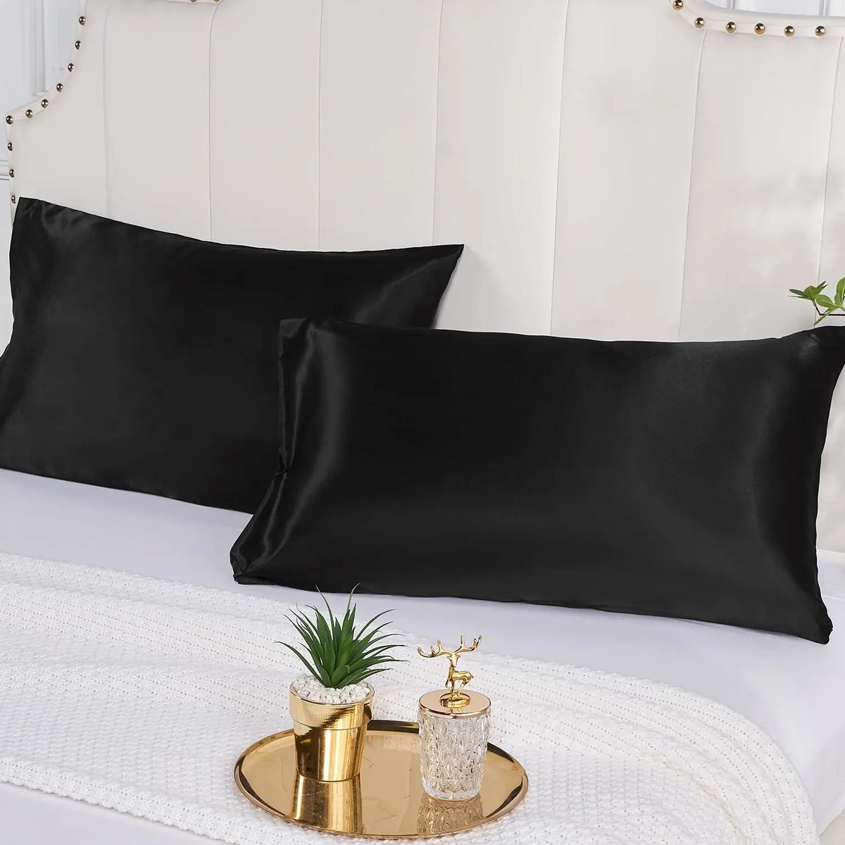 Black satin pillowcase set displayed on a white bed with gold decorative accents.