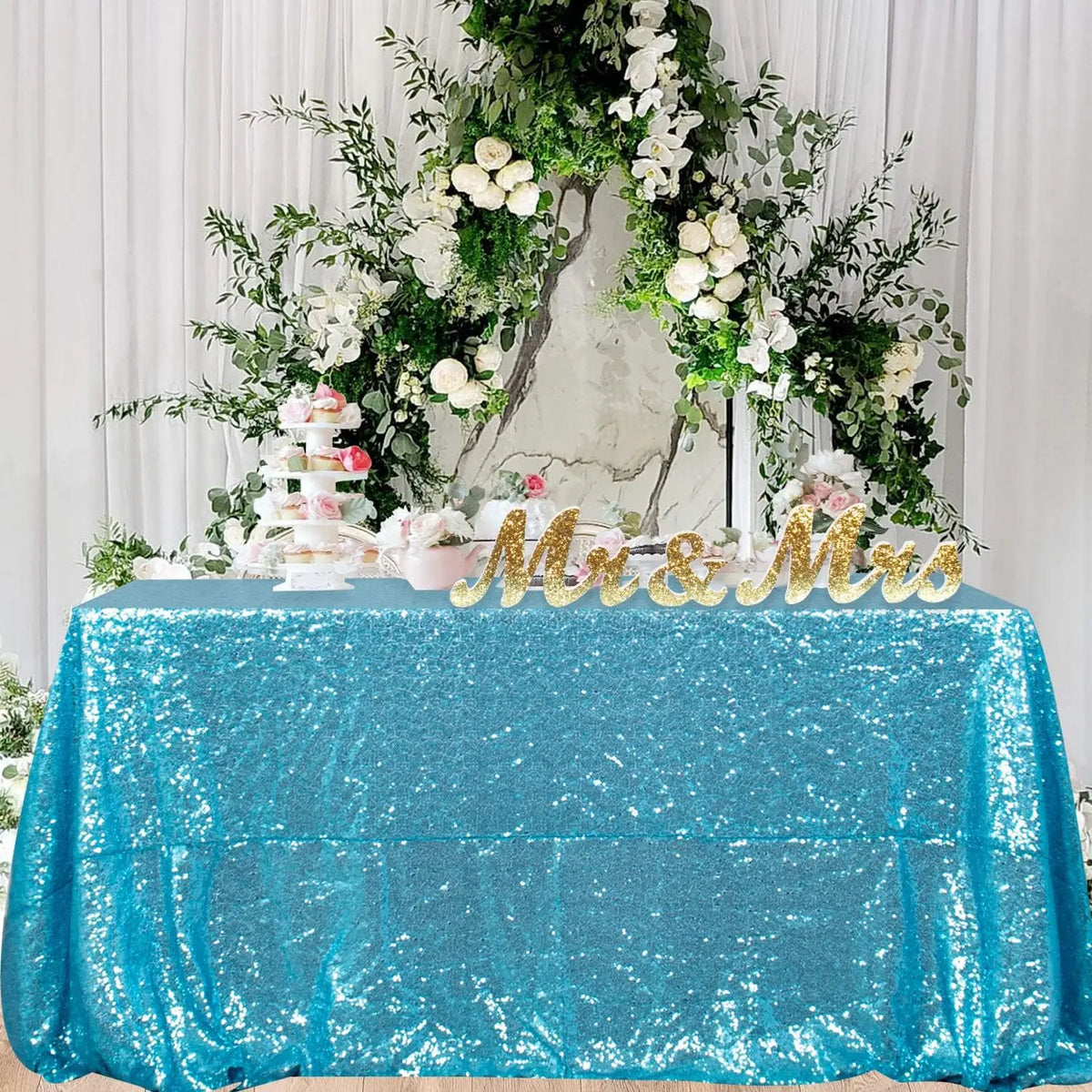 A turquoise sequin rectangle table cover is displayed with a floral and greenery centerpiece.