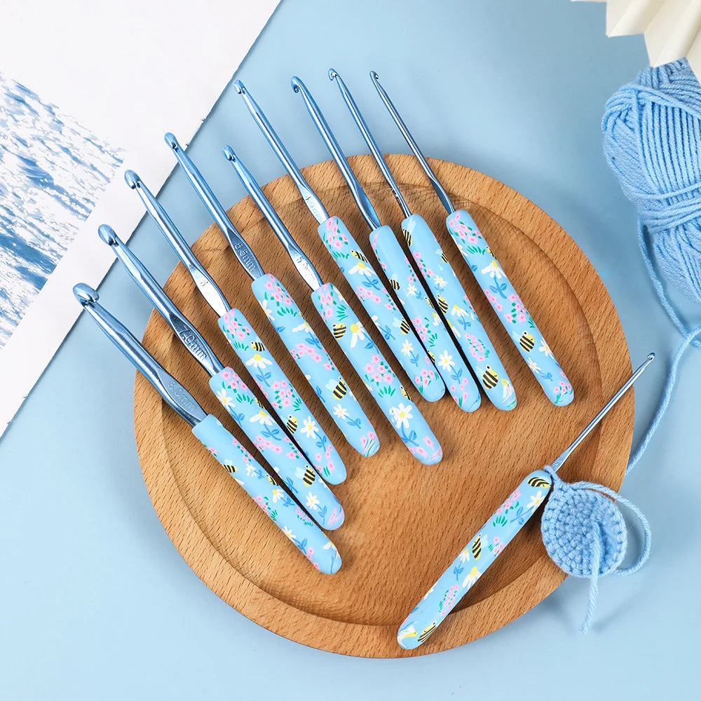 A wooden board holds a set of light blue and white ergonomic crochet hooks for knitting and weaving