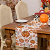 Linen table runner featuring an autumn harvest design with pumpkins and leaves on a wooden table.