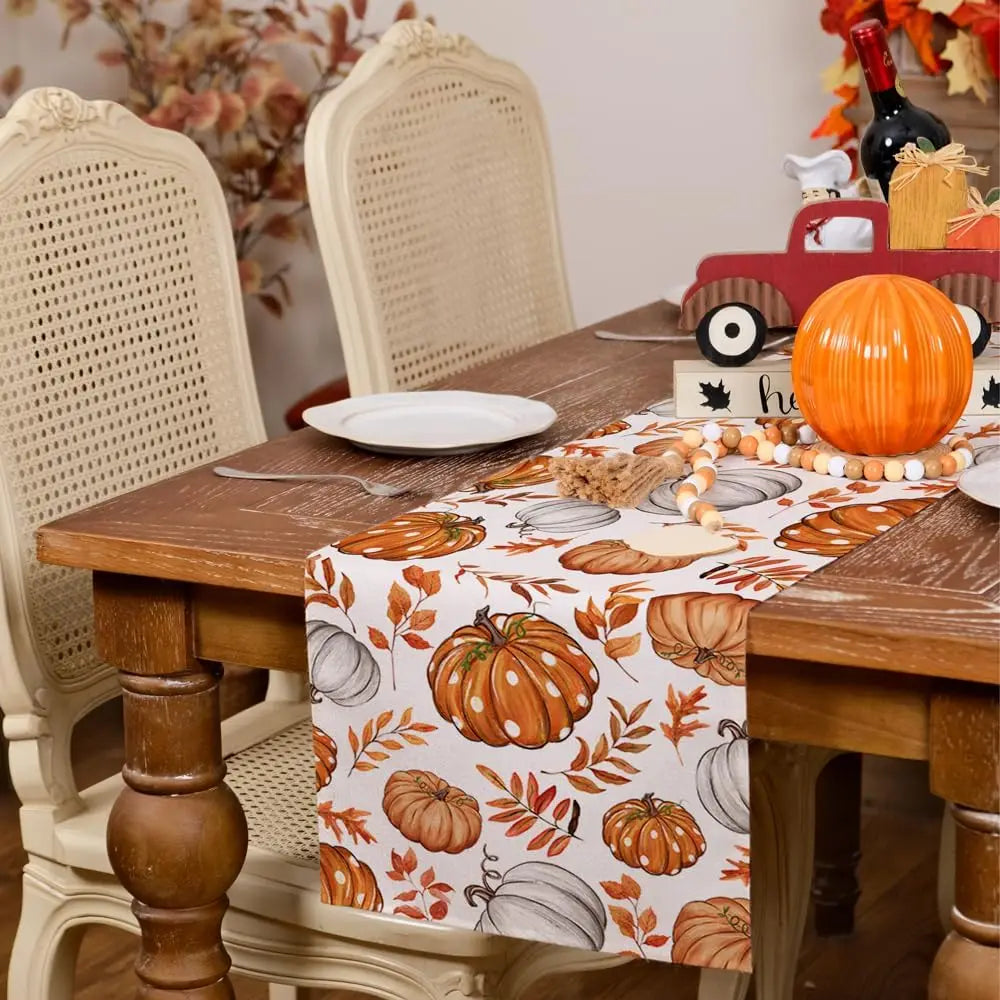 Linen table runner featuring an autumn harvest design with pumpkins and leaves on a wooden table.