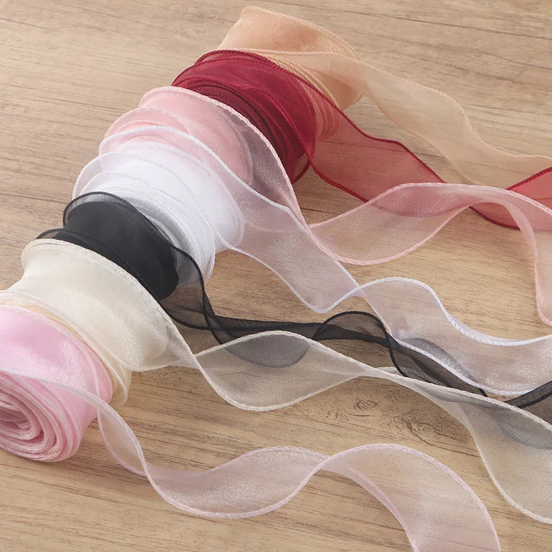 A collection of sheer satin ribbons in shades of pink, red, black, and nude are rolled and draped on a wooden surface.