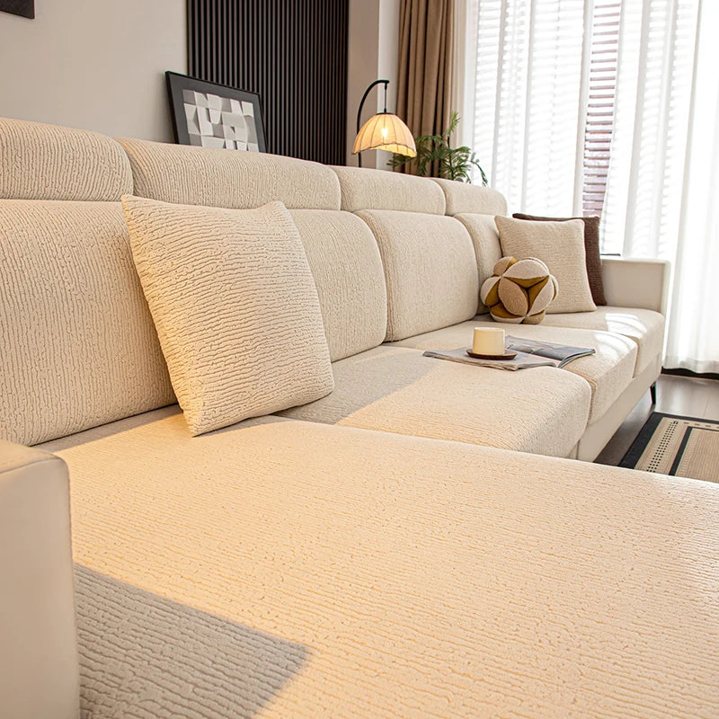 A beige stretch sofa seat cushion cover displayed on a light-colored sofa with decorative pillows and natural light.