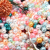 A close-up of various colored imitation pearl beads in pink, blue, gold, and green scattered on a white surface.