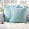 A light blue velvet decorative cushion cover with teal piping rests on a white knitted blanket.