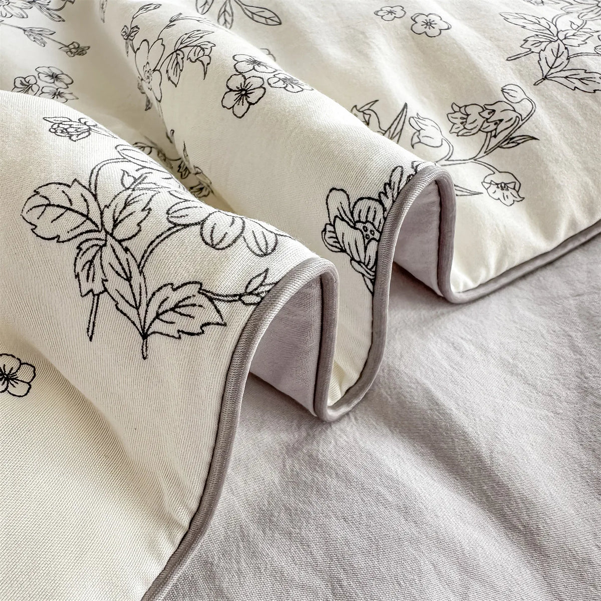 A close-up of a cream-colored quilt blanket with a black floral print folded on a light gray surface.