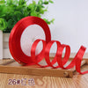 Red satin ribbon rolled on a wooden board with green foliage in the background