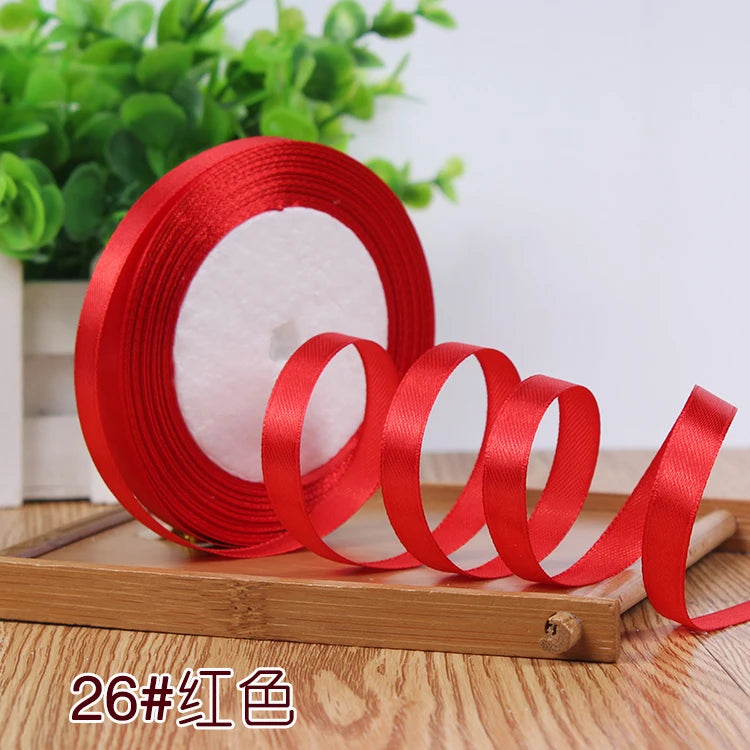 Red satin ribbon rolled on a wooden board with green foliage in the background