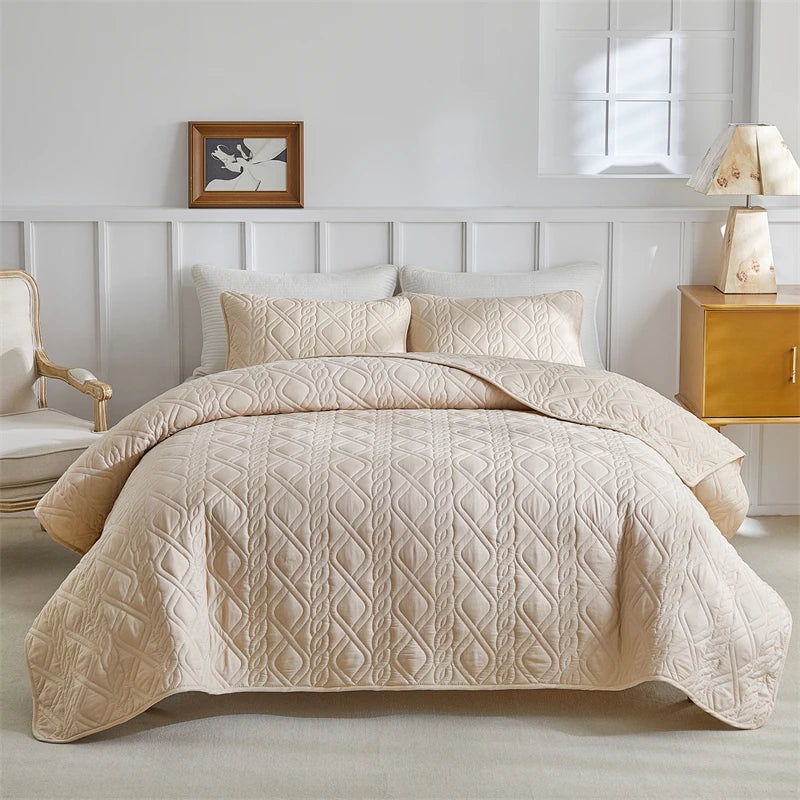 Light beige lightweight queen quilt bedding set displayed on a bed with white paneling and natural light.