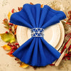 A bright blue fabric napkin tied into a decorative ring, placed on a white plate surrounded by autumn leaves.