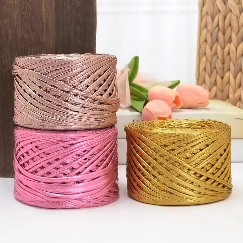 Three spools of metallic pink, magenta, and gold cake yarn for crafting