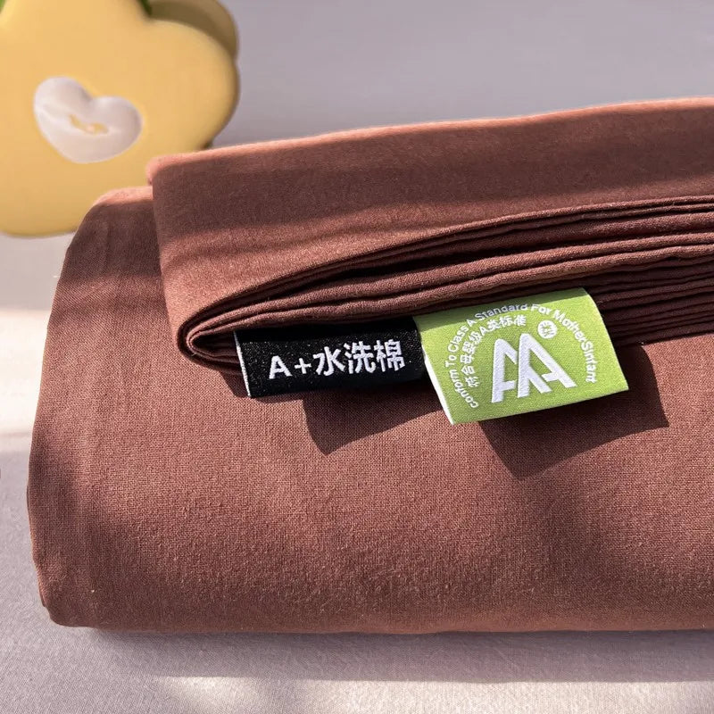 A rolled brown organic cotton bedding set with a green care tag is shown on a light surface.