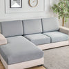 A modern light gray sofa with slipcovers sits in a bright room next to a framed motivational sign and a potted plant.
