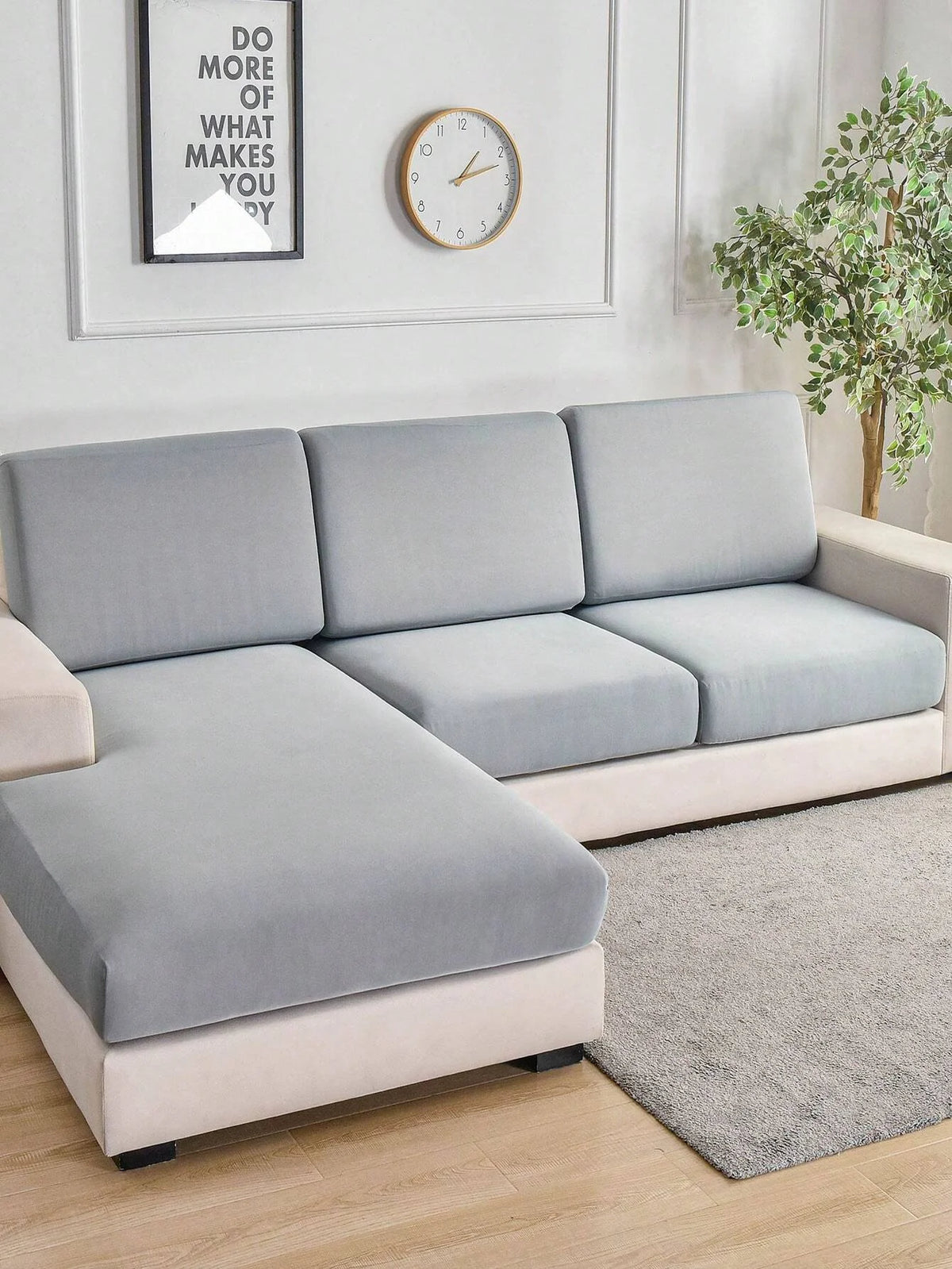 A modern light gray sofa with slipcovers sits in a bright room next to a framed motivational sign and a potted plant.