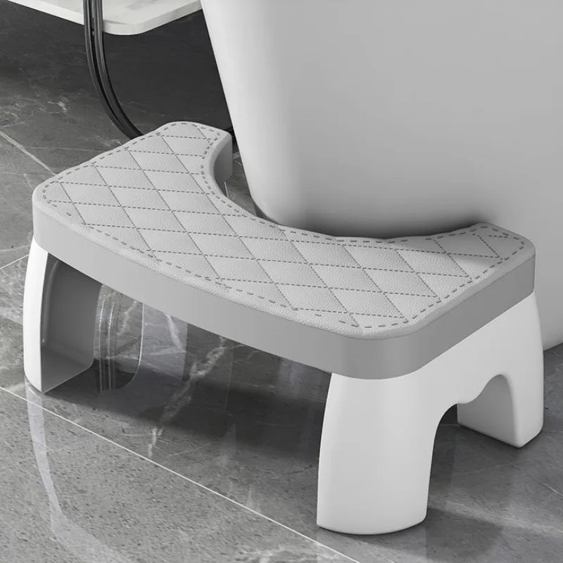 A white adjustable adult toilet squat stool with a padded seat and supportive legs is shown on a glossy floor.