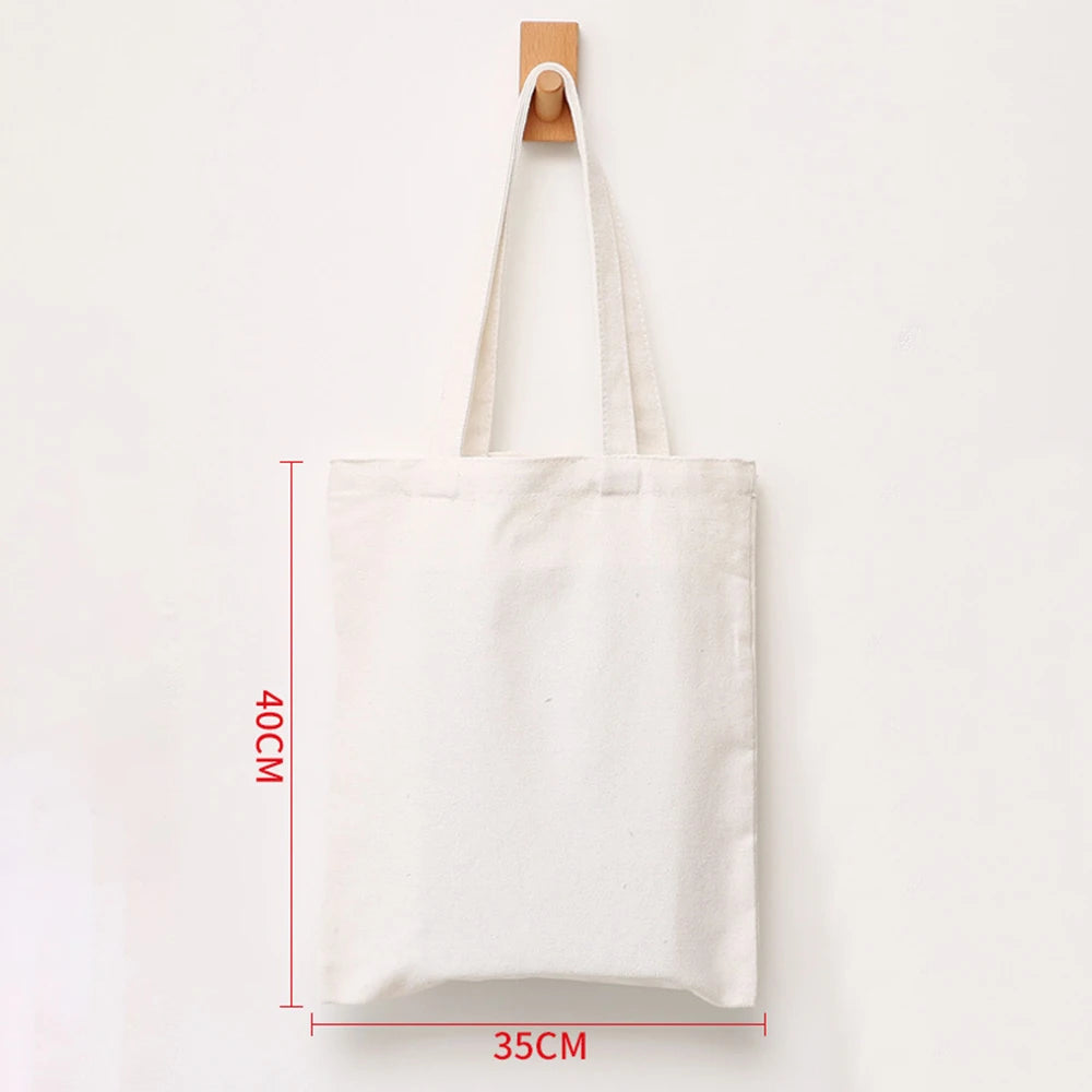 A white reusable canvas tote bag hanging on a wooden hanger against a white background.
