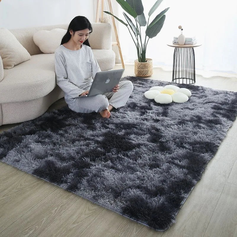 A dark gray faux fur rug with white decorative stones is placed on a light wood floor in a modern living room setting.