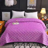 A purple plush velvet quilted bed cover blanket is displayed on a bed with white pillows and dark wall decor.