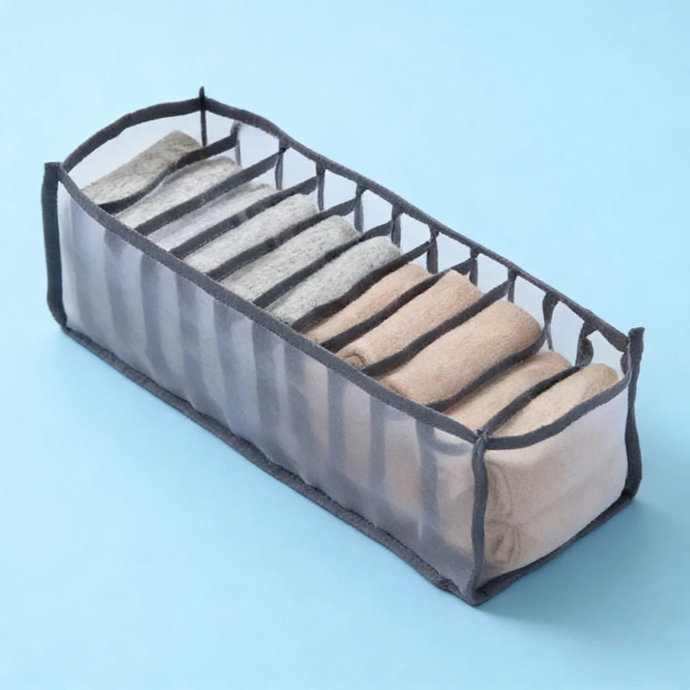 A clear mesh drawer organizer with vertical dividers holding folded gray and tan undergarments.
