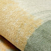 A close-up of a round rug featuring a gradient pattern of golden yellow transitioning to sage green.