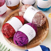 A collection of metallic fabric strip yarn in various shades including gold, pink, and purple, displayed on a wooden tray.