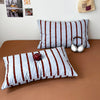 A set of striped duvet cover and pillowcases in white and brown stripes with a decorative pillow and headphones displayed on 
