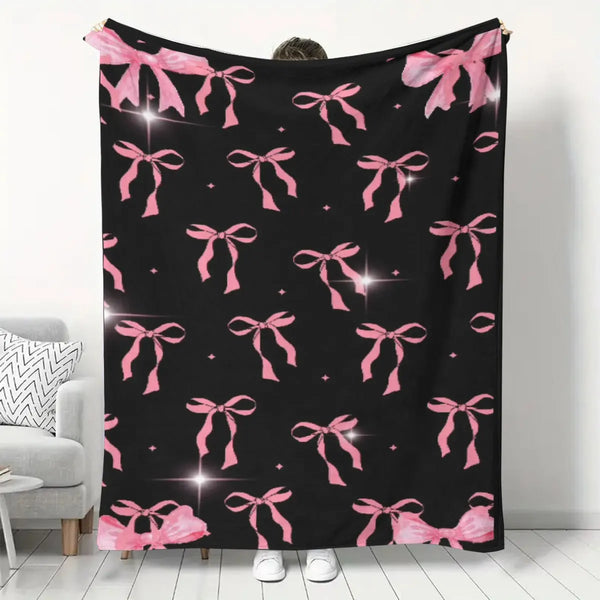 A black flannel blanket with a pink floral pattern featuring repeated bow motifs.