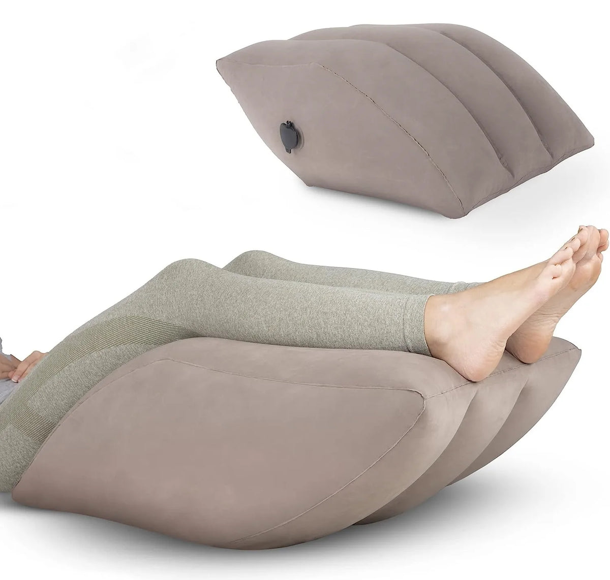 A beige inflatable leg elevation pillow shown in a storage bag, positioned under a person's foot.