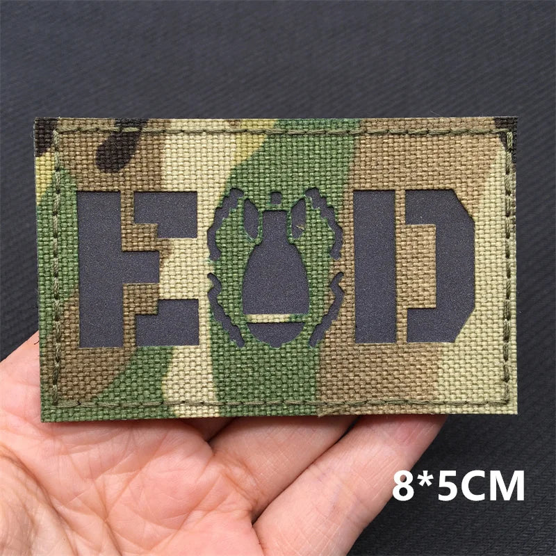 A rectangular tactical patch featuring the letters EOD in a camouflage pattern is held in a hand.