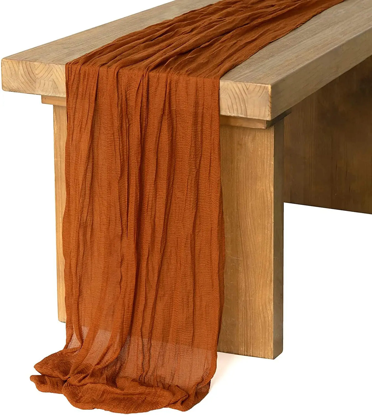 A rust orange rustic gauze table runner draped over a wooden table.