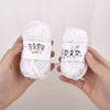 A pair of hands holds two balls of white milk cotton yarn for a crochet kit.