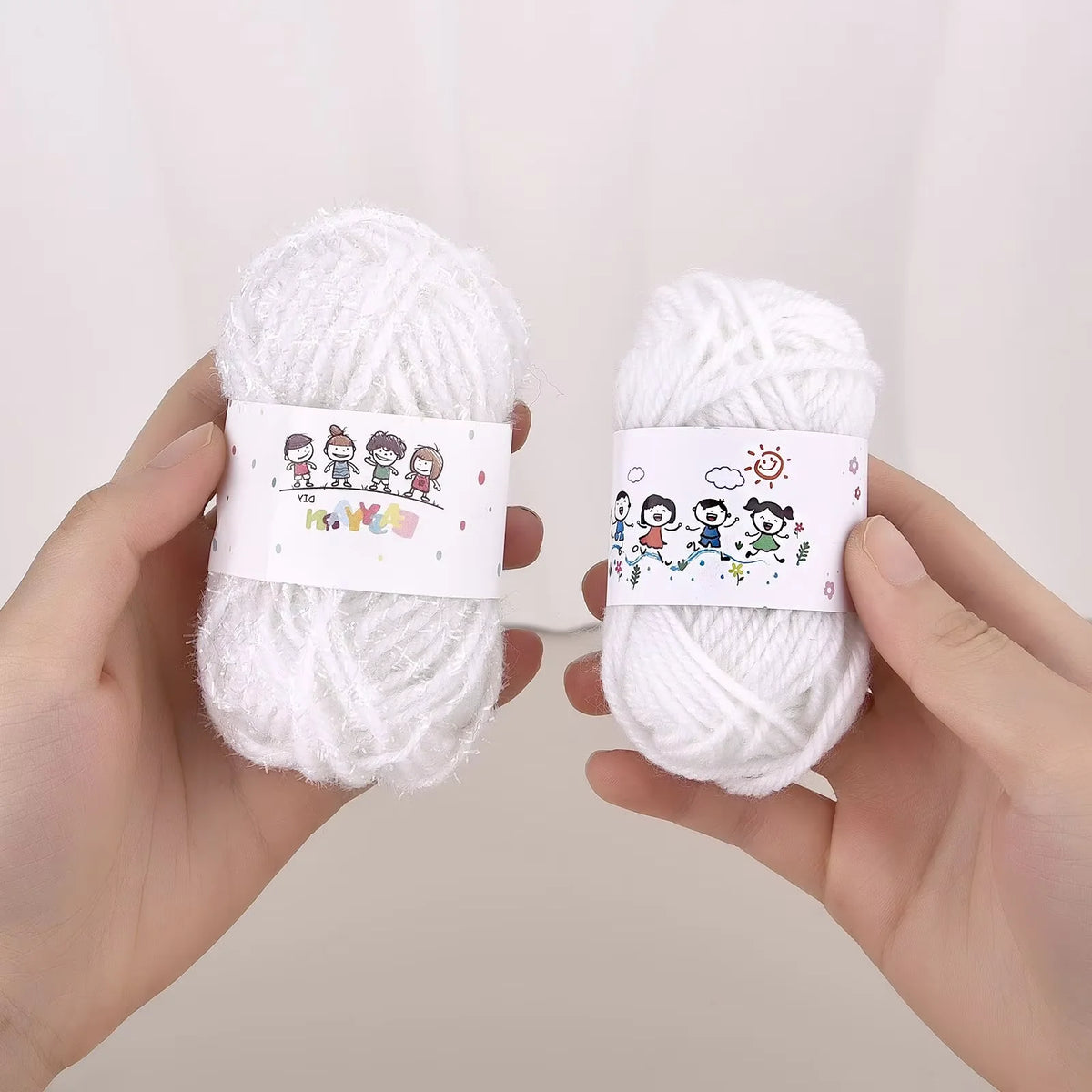 A pair of hands holds two balls of white milk cotton yarn for a crochet kit.