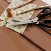 A pair of professional dressmaking pinking shears resting on a wooden surface with pencils and patterned paper.