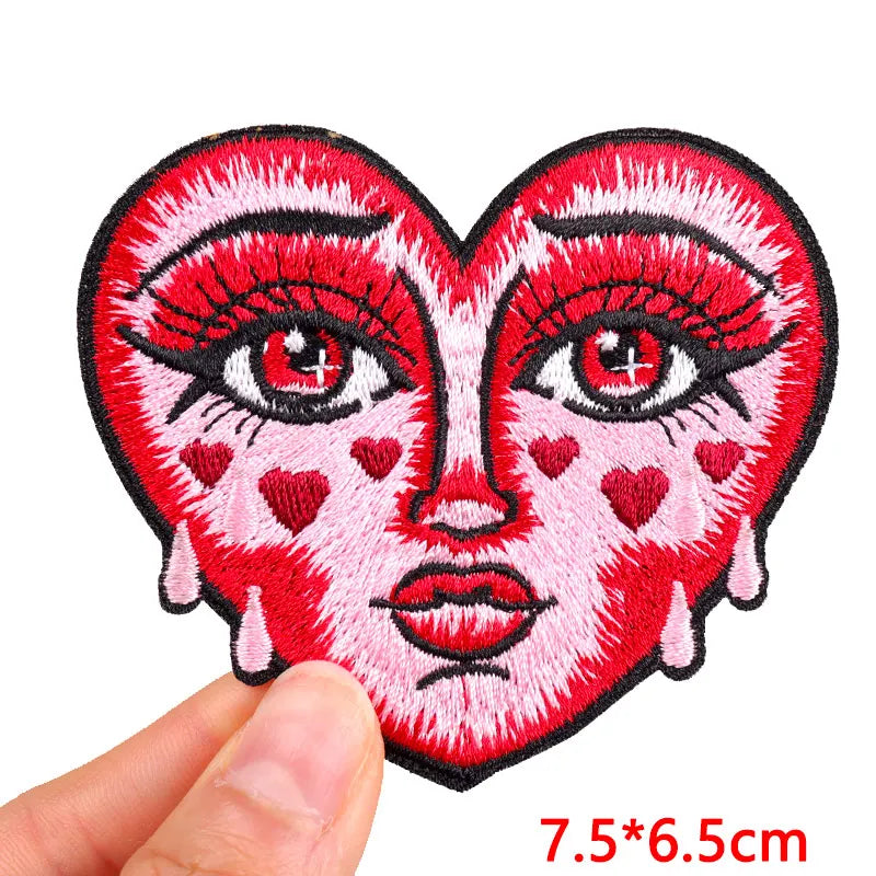 A red embroidery patch depicting a heart-shaped face with pink skin, red lips, and prominent eyelashes.