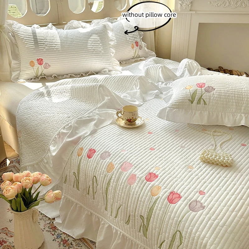 White quilted bedding set featuring pink and green floral embroidery on a duvet cover and pillows.