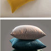 A stack of velvet throw pillows in shades of yellow, beige, teal, and dark green.